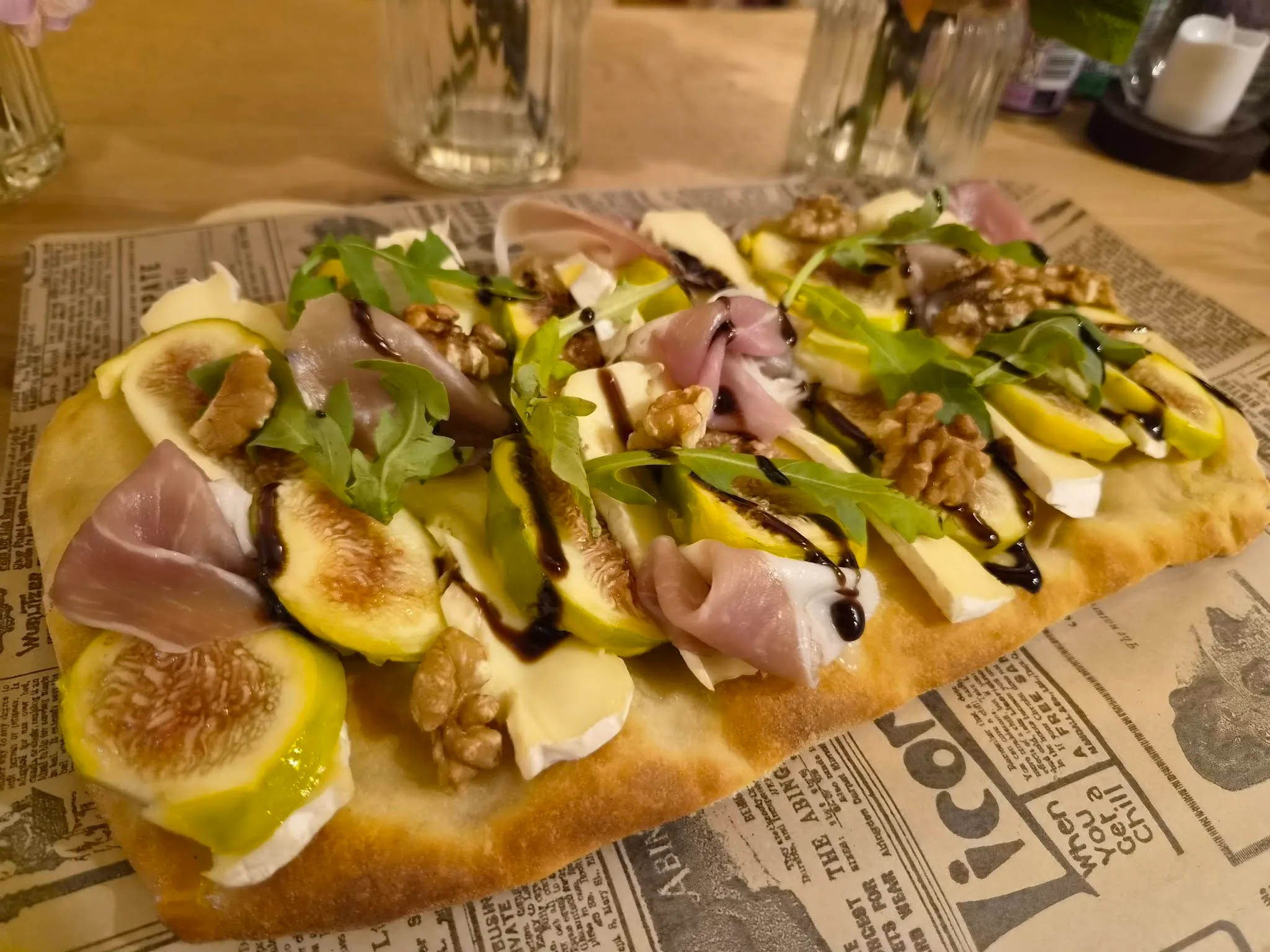 Fig, brie and prosciutto pinza with rocket and balsamic on a wooden table
