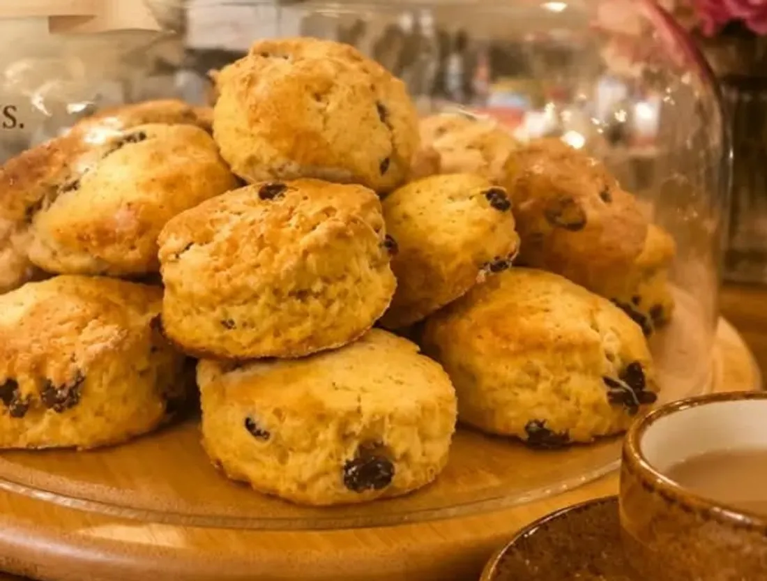 Freshly baked homemade scones under a glass cloche with tea and coffee
